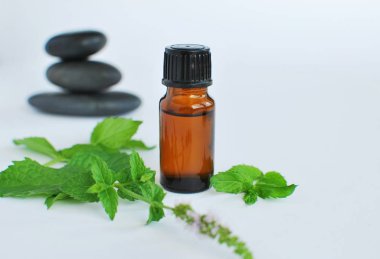 Kahverengi şişedeki nane yağı, spa taşları ve beyaz havlular..