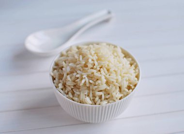 Seramik kaşıkla beyaz seramik kasede pilav pişirdim. Beyaz ahşap arkaplanda yakın plan görünümü