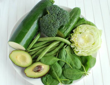 Beyaz tabakta yeşil doğal taze sebzeler. Vejetaryen yemeği. Beyaz ahşap arkaplanda üst görünüm.