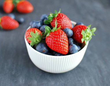 Beyaz seramik kasede taze meyveler. Yabanmersini ve çilek. Koyu kırsal arkaplanda yakın plan görünümü.