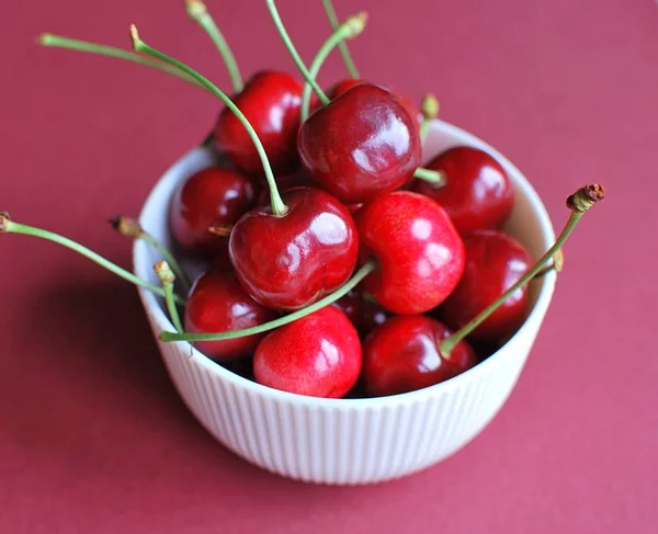 Fresh black cherries in bowl. Ripe cherry berries on red background.