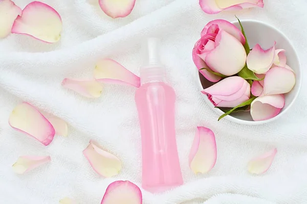 Natural rose water spray as facial toner, make up remover, roses petals in bowl on white towel, beauty, spa flat lay.