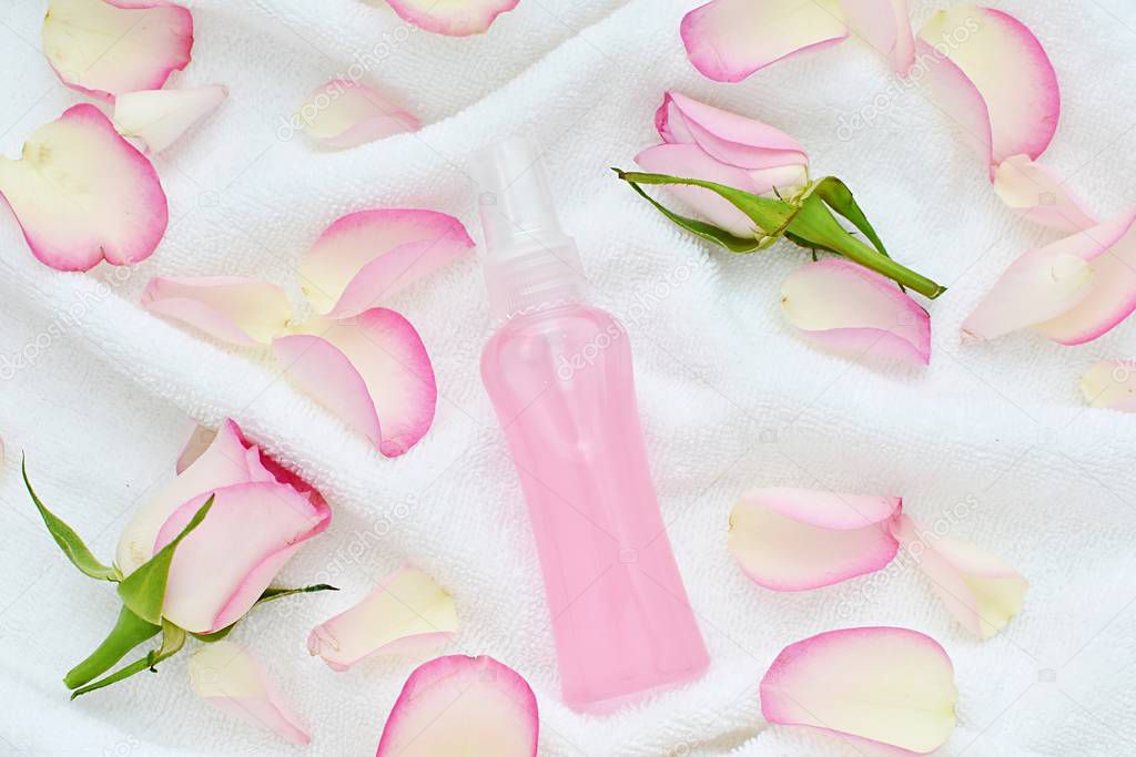 Natural rose water spray as facial toner, make up remover, roses petals in bowl on white towel, beauty, spa flat lay.