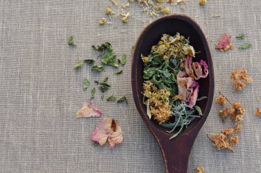 Ahşap kaşıkta doğal bitkisel ilaçlar için kurutulmuş otlar, keten kumaş üzerinde fotokopi alanı olan üst manzara. Ev hekimi, şifalı bitkiler..