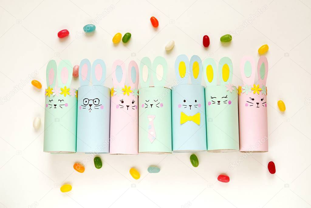 Happy Easter paper decorations, cute bunnies made from toilet paper roll, flat lay composition with colorful  candies, easy crafts for kids.