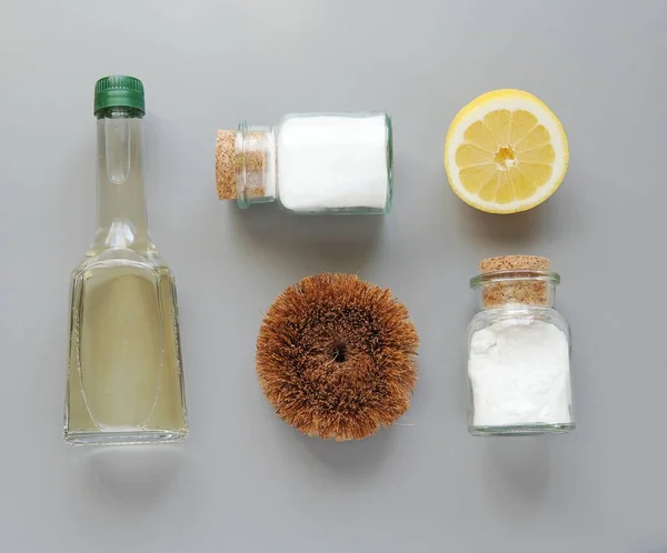 Zero waste home cleaning products, vinegar, salt, baking soda, lemon and coconut brush, flat lay composition on gray background.