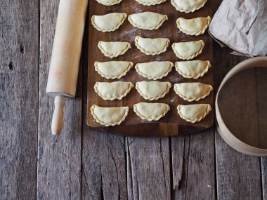 On the kitchen cutting board, ready-made dumplings with ingredients for making dough and various kitchen utensils. clipart