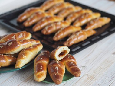 Fırından çıkan siyah bir ekmek tepsisinin üzerinde ev yapımı kızarmış simit. Yemek hazır. Susam tohumları serpiştirilmiş. Ev mutfağı.