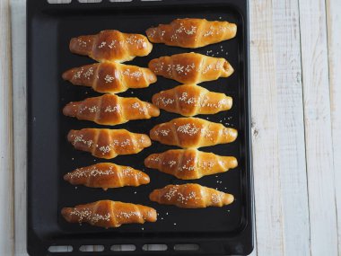 Fırından çıkan siyah bir ekmek tepsisinin üzerinde ev yapımı kızarmış simit. Yemek hazır. Susam tohumları serpiştirilmiş. Ev mutfağı.