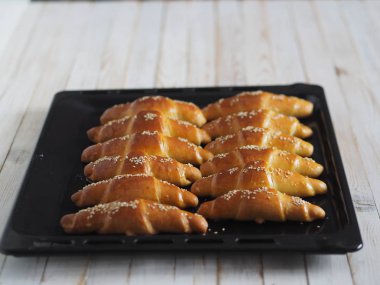 Fırından çıkan siyah bir ekmek tepsisinin üzerinde ev yapımı kızarmış simit. Yemek hazır. Susam tohumları serpiştirilmiş. Ev mutfağı.