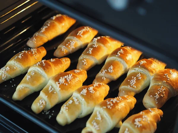 Ready-made toasted homemade bagels on a black baking sheet from the oven. Ready to eat. Sprinkled with sesame seeds. Home kitchen. — Stock Photo, Image