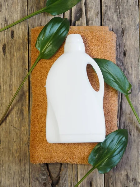 Koncepcja naturalnego ekologicznego detergentu do prania do łazienki. Zielone liście tropikalnej rośliny i butelka detergentu na ręczniku kąpielowym. Drewniane starożytne tło. Zdjęcie artystyczne. — Zdjęcie stockowe