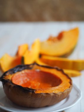 Balkabağı pişiriyorum. Ev yemekleri, vejetaryenler için doğal yiyecekler. Geleneksel sonbahar balkabağı yemekleri. Baharatlı ızgara balkabağı ve beyaz ahşap bir masada çiğ balkabağı..