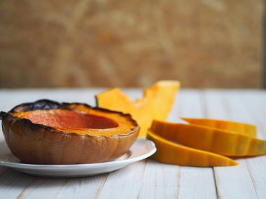 Balkabağı pişiriyorum. Ev yemekleri, vejetaryenler için doğal yiyecekler. Geleneksel sonbahar balkabağı yemekleri. Baharatlı ızgara balkabağı ve beyaz ahşap bir masada çiğ balkabağı..