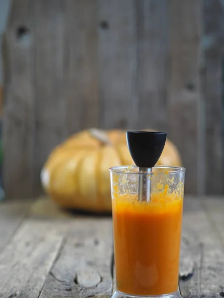 Grande abóbora redonda em uma mesa de madeira rústica. Purê de abóbora em um liquidificador. Cozinha caseira . — Fotografia de Stock