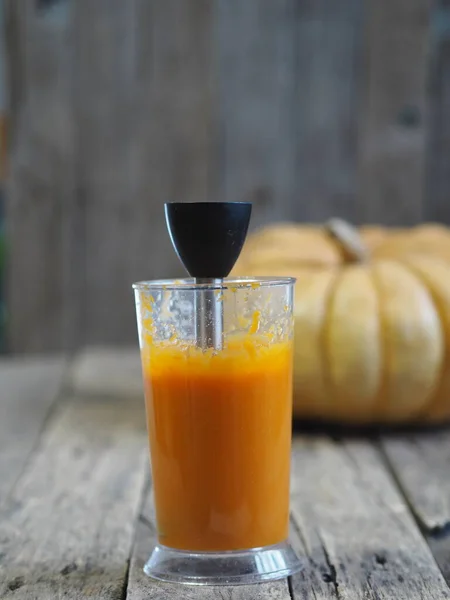 Grande abóbora redonda em uma mesa de madeira rústica. Purê de abóbora em um liquidificador. Cozinha caseira . — Fotografia de Stock