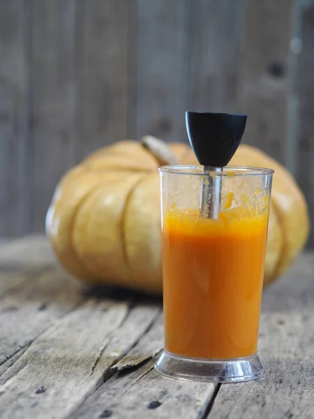 Grote ronde pompoen op een rustieke houten tafel. Pompoenpuree in een blender. Thuis koken. — Stockfoto