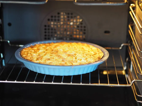 An open homemade pie with apples and red currants is cooked in a black oven. Home cooking. — Stock Photo, Image