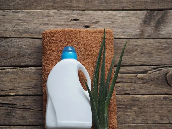 Η έννοια των οικολογικών φυσικών απορρυπαντικών. Ένα πλαστικό λευκό μπουκάλι απορρυπαντικού σε λευκά είδη μπάνιου με ένα φαρμακευτικό φυτό αλόη βέρα. Ξύλινο αρχαίο φόντο. Χωριό. — Φωτογραφία Αρχείου