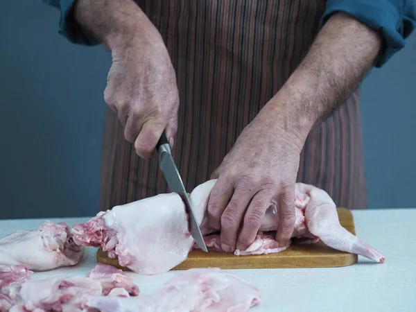 Un chef masculin tient un couteau et coupe en morceaux de viande de lapin crue sur une planche à découper de cuisine . — Photo