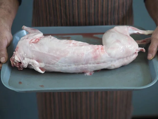 Um chef masculino está segurando uma carne crua de coelho em uma bandeja de carcaça. Vai cortar em pedaços . — Fotografia de Stock