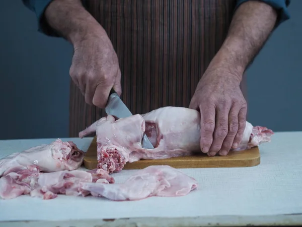 Un chef masculino sostiene un cuchillo y corta en trozos carne cruda de conejo en una tabla de cortar la cocina . — Foto de Stock