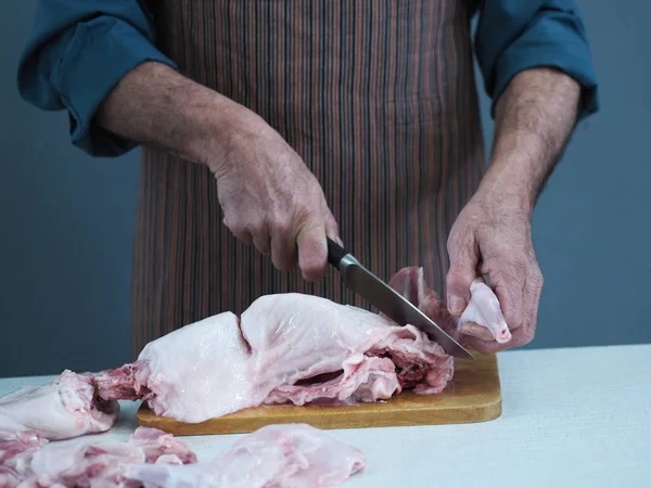 Un chef masculino sostiene un cuchillo y corta en trozos carne cruda de conejo en una tabla de cortar la cocina . — Foto de Stock