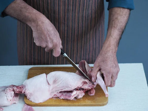 Un chef masculino sostiene un cuchillo y corta en trozos carne cruda de conejo en una tabla de cortar la cocina . — Foto de Stock