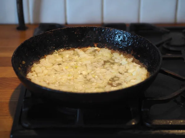 家庭料理。ストーブの上に黒い鍋に油で玉ねぎを揚げた。近くの揚げ魚。パイの充填の準備の段階. — ストック写真