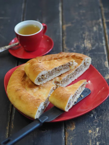 Cocina casera. Un pastel redondo con col y lucio de pescado de río en un plato rojo sobre una mesa negra antigua. Cocinar en casa. Una pequeña celebración . — Foto de Stock