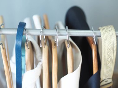 Erkek ve kadın kıyafetlerinin olduğu askılar. Gri arkaplanda açık ve mavi elbiseler.