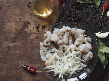 XE salad of freshly salted river pike fish on a cutting kitchen board with ingredients for cooking. Pike fillet pieces. Wooden brown background.