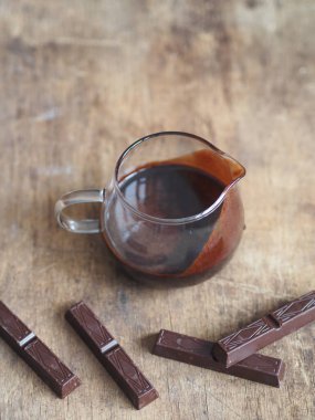 Şekerlemeler için sıcak çikolata kreması. Tahta bir arka planda çikolata parçaları..