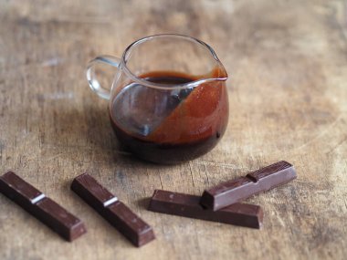 Şekerlemeler için sıcak çikolata kreması. Tahta bir arka planda çikolata parçaları..