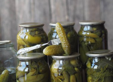 Konserve salatalık turşusunun faydaları ve zararları. Çatal üzerinde ev yapımı salatalık turşusu ve tahta bir arka planda kavanozlar. Yan görüş. Metin için yer.