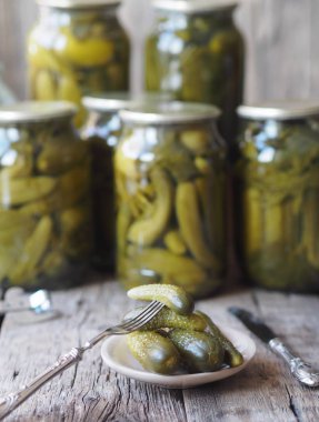 Konserve salatalık turşusunun faydaları ve zararları. Çatal üzerinde ev yapımı salatalık turşusu ve tahta bir arka planda kavanozlar. Yan görüş. Metin için yer.