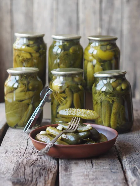 The benefits and harms of canned pickled cucumbers. Homemade pickled cucumbers on a fork and in jars on a wooden ancient background. Side view. Place for text.