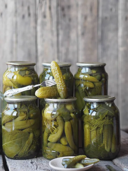 The benefits and harms of canned pickled cucumbers. Homemade pickled cucumbers on a fork and in jars on a wooden ancient background. Side view. Place for text.