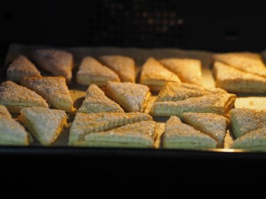 Ekmek arası üçgen için ev yapımı puf böreği fırında siyah bir fırın tepsisi üzerinde. Şeker ve beyaz susam tohumu serpiştirilmiş. Tatil için hazırlanıyor..