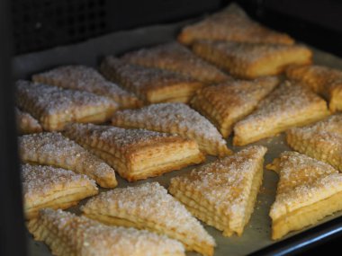 Ekmek arası üçgen için ev yapımı puf böreği fırında siyah bir fırın tepsisi üzerinde. Şeker ve beyaz susam tohumu serpiştirilmiş. Tatil için hazırlanıyor..