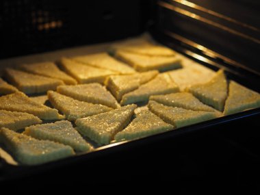 Ekmek arası üçgen için ev yapımı puf böreği fırında siyah bir fırın tepsisi üzerinde. Şeker ve beyaz susam tohumu serpiştirilmiş. Tatil için hazırlanıyor..