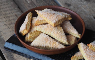Tahta arka planda kahverengi bir tabakta ev yapımı kurabiye puf böreği üçgeni. Yan görüş. Metin için yer. Üzerinde beyaz susam ve şeker var..