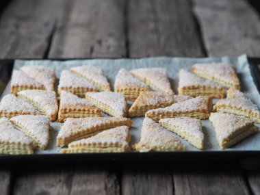 Fırından çıkan siyah bir tepside ev yapımı sandviç böreği çikolatalı kurabiyeler. Eski ahşap kırsal masa. Yukarıdan bak. Şeker ve beyaz susam tohumları serpiştirilmiş..