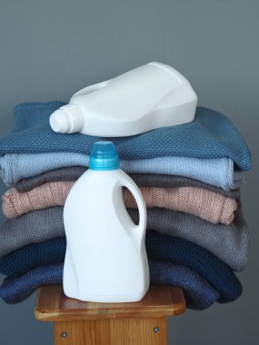 Deterjan için beyaz plastik şişeler ya da nazik, çevre dostu bir yıkama için jel. Beyaz plastik bir rafta kalın örgü giysiler var. Mavi gri beyaz tonlar. Gri arkaplan.