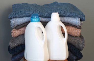 Deterjan için beyaz plastik şişeler ya da nazik, çevre dostu bir yıkama için jel. Beyaz plastik bir rafta kalın örgü giysiler var. Mavi gri beyaz tonlar. Gri arkaplan.