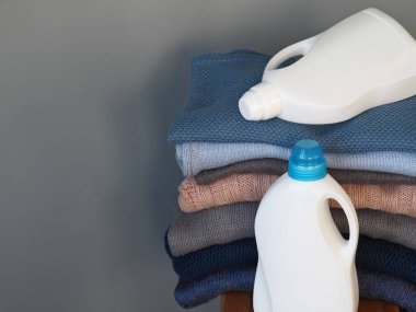 Deterjan için beyaz plastik şişeler ya da nazik, çevre dostu bir yıkama için jel. Beyaz plastik bir rafta kalın örgü giysiler var. Mavi gri beyaz tonlar. Gri arkaplan.