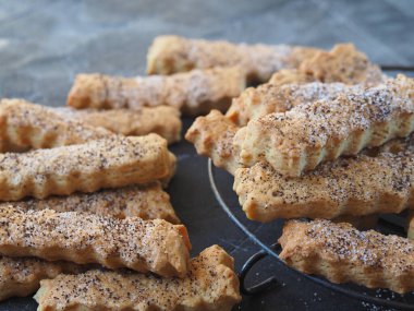 Ev yemeği. Siyah arka planda metal bir ızgaraya şeker ve haşhaş tohumu serpiştirilmiş Shortbread Sticks. Yakın plan, kenar görünüm.