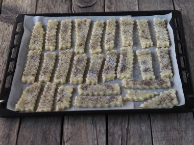 Ev yemeği. Ahşap bir masanın üzerinde mutfak fırınından çıkan siyah bir ekmek. Tereyağlı kurabiyeler şeker ve haşhaş tohumları serpiştiriyor..