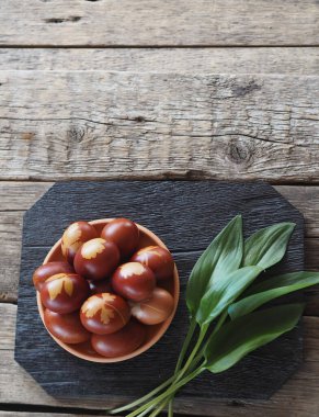 Renkli yumurtalı Paskalya arkaplanı. Renkli yumurtalar soğan kabuğundan tütsülenmiş. Tahta bir arka planda, koyu renk bir tahtada yaprakları var. Mesaj için yer var..