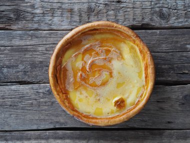 Ev yapımı fırınlanmış peynirli kek, balkabağından yapılmış, çırpılmış yumurtaların üzerine şeker dökülmüş, ahşap bir arka planda. Yakın plan, üst görüş. Mesaj için yer..